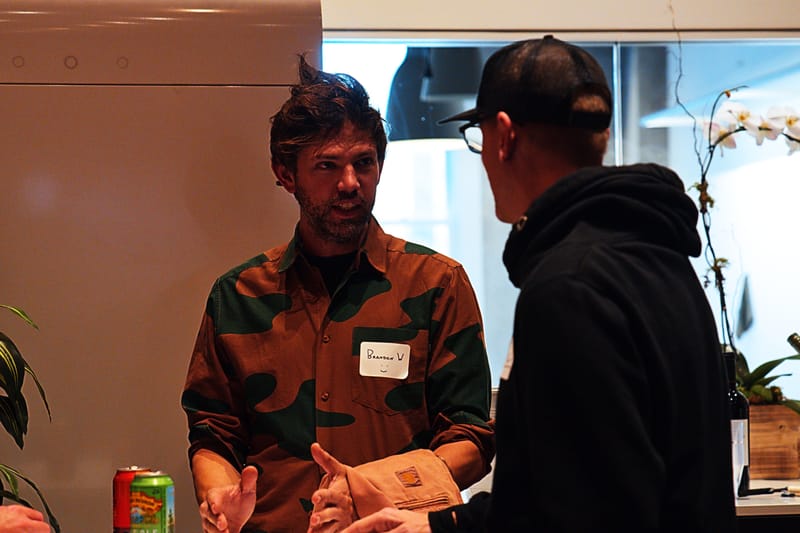 Two attendees talking beside a white orchid, one in a camouflage shirt with a handwritten name tag.